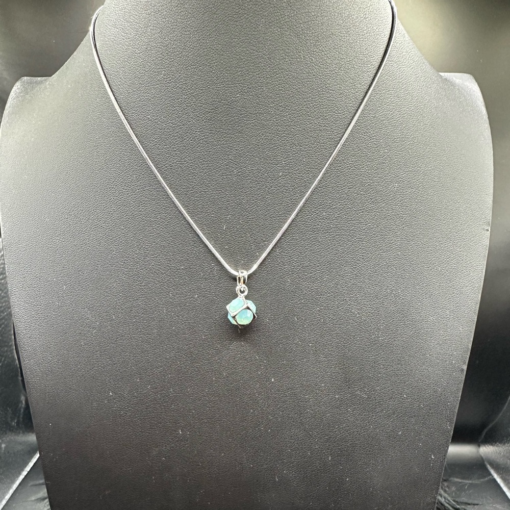 Round light blue crystal incased in a silver square on a silver chain.